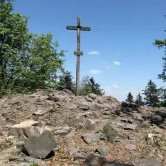 Kamienisty szczyt z drewnianym krzyżem, otoczony drzewami. Idealne miejsce na wędrówkę po górach świętokrzyskich szlaki.