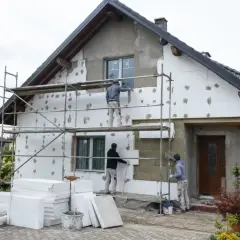 Trwa ocieplanie domu. Pracownicy na rusztowaniach nakładają tynk. Sprawdź, jaka jest cena ocieplenia za 1m2 robocizna.