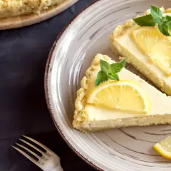 Dos porciones de tarta de limón, decoradas con rodajas de limón y hojas de menta, listas para ser disfrutadas.