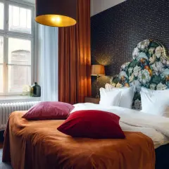 Ett lyxigt rum på nofo hotell Stockholm med en stor säng, blommig huvudgavel och orangea sammetsgardiner.