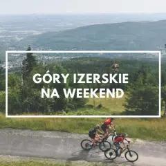 Trzech rowerzystów przemierza malownicze szlaki w Górach Izerskich w Polsce. W tle widać kolejkę gondolową i rozległy krajobraz.