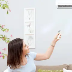 Mujer ajusta el aire acondicionado con control remoto. El vane del aire acondicionado significa confort y frescura en casa.
