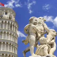 Kamienna rzeźba dzieci trzymających herb z napisem "PISA" na tle Krzywej Wieży w Pizie.