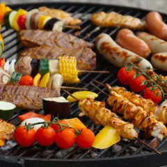 Un festin de Noël en plein air : brochettes de poulet, saucisses, steaks et légumes colorés sur un barbecue.