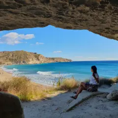 Mujer sentada en una cueva, contemplando la playa y el mar azul. Un lugar idílico que ver cerca de Cabo de Gata.