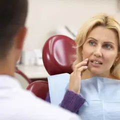 Kobieta w gabinecie dentystycznym, dotykając policzka, jakby śniło jej się o ruszającym się zębie.