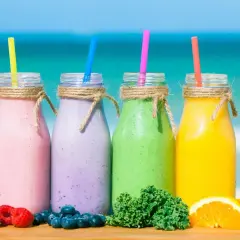 Cztery kolorowe smoothie na plaży: różowe, fioletowe, zielone i żółte. Idealne na lato, pokazują, jak zrobić smoothie z owoców i warzyw.