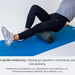 Kobieta wykonuje rolowanie przywodzicieli na macie z użyciem czarnego rollera z zielonymi kropkami.