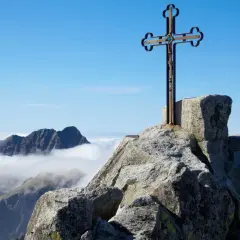 Krzyż na skalistym szczycie, najwyższy szczyt Tatr, góruje nad morzem chmur.