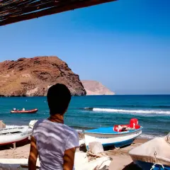 Persona contempla la **playa Las Negras** con barcas en la arena y el mar azul. Montañas áridas al fondo.