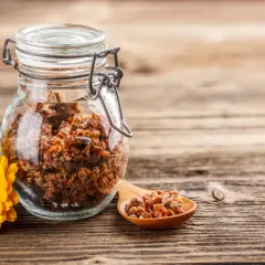 Propoli grezza in un barattolo di vetro, con un cucchiaino e un fiore giallo. Scopri come usarla per il benessere.