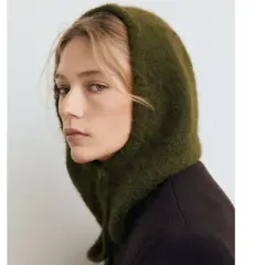 Mujer con un balaclava verde de lana, cubriendo su cabeza y cuello, con un abrigo oscuro.