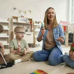 Nauczycielka prowadzi zajęcia z dziećmi, które grają na instrumentach. Wszyscy bawią się, używając zabawki muzyczne dla dzieci.