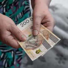 Dwie stuzłotowe banknoty w dłoniach, symbolizujące wsparcie finansowe, być może zasilek pielegnacyjny.