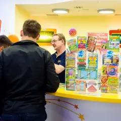 Mężczyźni stoją przy ladzie, na której widać wiele zdrapek Lotto. Czy na Orlenie są zdrapki Lotto? Tak, jak widać na zdjęciu.
