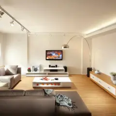 Iluminar un salón moderno con focos dirigibles y una lámpara de arco. Sofás grises, mesa de centro blanca y mueble de TV.
