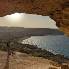 Frauenblick auf die Bucht von Malta im Dezember. Das Wetter ist mild, die Sonne scheint, und die Wellen brechen am Strand.