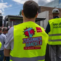 Menschen in Warnwesten mit der Aufschrift "ZUSAMMEN HANDELN FÜR BESSERE TARIFE!" bei Tarifverhandlungen im Einzelhandel.