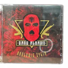 Okładka płyty CD "Królowie życia" zespołu Gang Albanii. Czerwona kominiarka z orłem, złote kałasznikowy i mroczne tło.