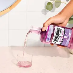Ręka wylewa fioletowy płyn Listerine Total Care Extra Mild do szklanki. Poznaj listerine skład i ciesz się świeżym oddechem.