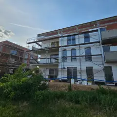 Budowa nowych bloków mieszkalnych, widać rusztowania i izolację. Słońce przebija się przez chmury.