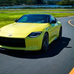 Gul Nissan 400Z kör på en kurvig bana med grönskande fält och träd i bakgrunden.