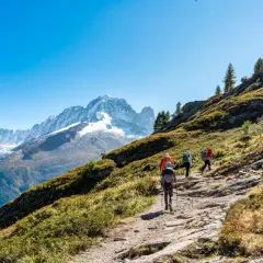Senderismo en Francia, un grupo de excursionistas asciende por un sendero rocoso con vistas a picos nevados y un glaciar.