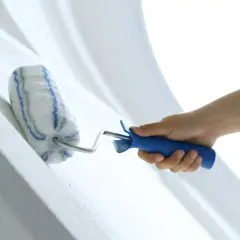 Hand streicht mit einer Farbrolle über eine weiße Wand. Der Putz wird frisch gestrichen.