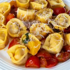 Talerz pełen tortellini z pomidorkami koktajlowymi i startym parmezanem.