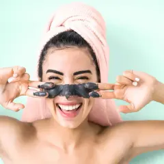 Ragazza felice con maschera viso nera, si chiede quante volte a settimana usarla per una pelle radiosa.