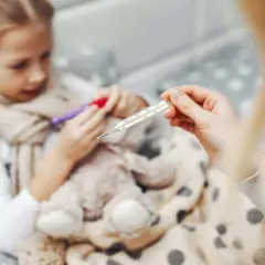 Dziecko z gorączką, objawy rotawirusa. Mama mierzy temperaturę termometrem.