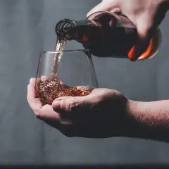 Une main verse un liquide ambré dans un verre, peut-être le pire whisky jamais goûté.