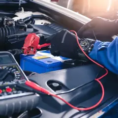Sprawdzanie akumulatora za pomocą multimetru. Mechanik w rękawiczkach podłącza przewody, by sprawdzić, jak sprawdzić czy prostownik jest sprawny.