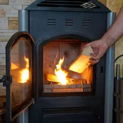Ein Mann legt Holz in einen brennenden Kamin. Ab wann brennt Holz? Sobald es trocken ist und Zündmaterial vorhanden ist.