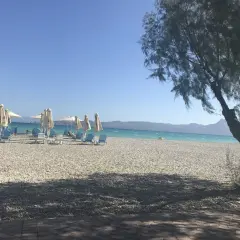 Słoneczny dzień na plaży Alkyon. Białe leżaki i parasole czekają na plażowiczów. W tle turkusowe morze i góry.