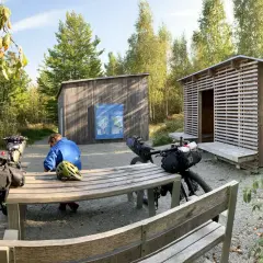 Cykelturist vilar vid rastplats i Åsnen nationalpark. Två packade cyklar står vid ett bord och bänkar.