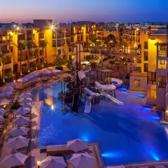 Wieczorem w Steigenberger Aqua Magic, basen z atrakcjami wodnymi i zjeżdżalniami, otoczony hotelowymi budynkami i leżakami pod parasolami.