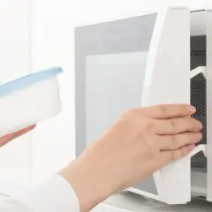 Ręka wkłada pojemnik do kuchenki mikrofalowej. Ten papier w mikrofali jest gotowy do podgrzania.