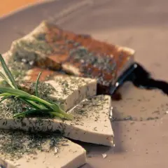Queso tofu marinado con hierbas y romero, servido en un plato con salsa oscura.