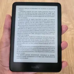 Main tenant un appareil Kindle format e-reader, affichant un texte en français sur fond noir.