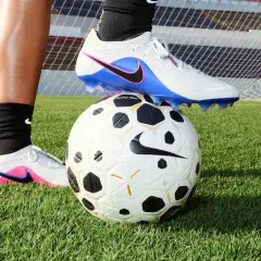 Un pied en crampons de foot, posé sur un ballon, sur l'herbe. Peut-on laver des chaussures de foot en machine ?