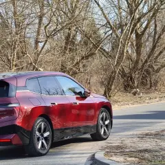 Czerwony BMW iX jedzie drogą, zbliżając się do znaku informującego o zakazie tonażowym 2,5 tony na dystansie 100m.