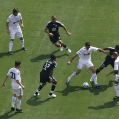 Piłkarze w białych strojach walczą o piłkę na zielonej murawie. To emocjonujący mecz, prawdziwy football po polsku!