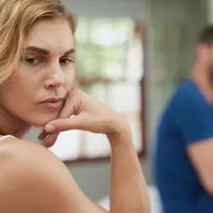 A woman looks worried, with a man blurred in the background.