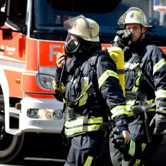 Zwei Feuerwehrmänner in voller Montur vor einem roten Feuerwehrauto. Sie sind bereit für den Einsatz. Wie viel verdient man als Feuerwehrmann?