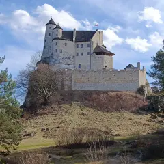 Zamek Bobolice na wapiennym wzgórzu, otoczony drzewami, pod błękitnym niebem z chmurami.