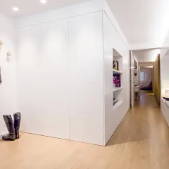Un recibidor panelado moderno con suelo de madera, estanterías empotradas, un sombrero y bufanda colgados, y botas de montar.