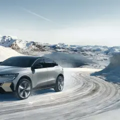 Voiture électrique avec pompe à chaleur traversant un paysage hivernal enneigé, montagnes et lac gelé en arrière-plan.