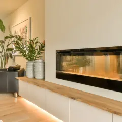 Nowoczesny biokominek w salonie inspiracje: czarna skórzana kanapa, wysokie rośliny i minimalistyczna zabudowa tworzą przytulną atmosferę.