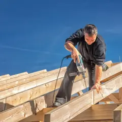 Budowniczy montuje drewniane elementy konstrukcji dachu, przygotowując przedłużenie okapu.